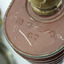 Top of red/brown tin cannister showing detail of inscription and cylindrical hose connected to the the top.