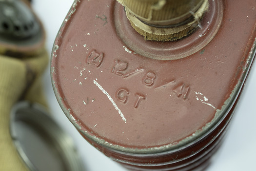 Top of red/brown tin cannister showing detail of inscription and cylindrical hose connected to the the top.