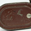 Oval shaped base of red/brown tin canister showing detail of inscription, signs of wear and tear with scratches. White round sticker with black text "136".