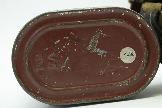 Oval shaped base of red/brown tin canister showing detail of inscription, signs of wear and tear with scratches. White round sticker with black text "136".