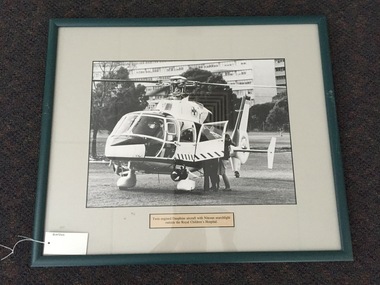 Photograph, framed, Twin engined Dauphine aircraft (helicopter) with Nitesun searchlight outside the Royal Childrens Hospital