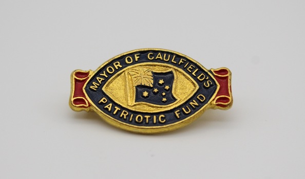 Small oval brass and enamel commemorative pin. Centre oval has blue enamel Australian flag, surrounded by the inscription "MAYOR OF CAULFIELD'S PATRIOTIC FUND". Red enamel scroll motif at rear. C-clasp fastening on reverse.
