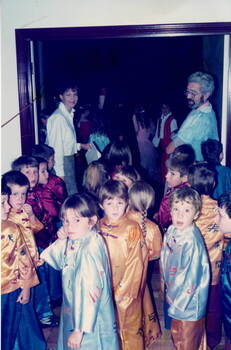 A lady and a man supervising group of children dressed in Chinese costumes waiting to enter a room .