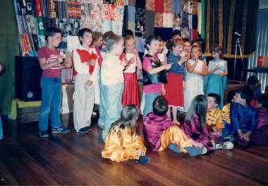 A choir of twenty young children singing on a stage. 