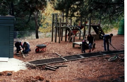 Three children and two adults working on playground equipment. 