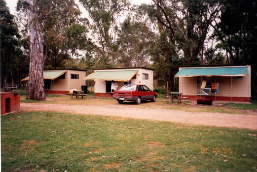 Three cabins and a barbecue in a bushland setting.