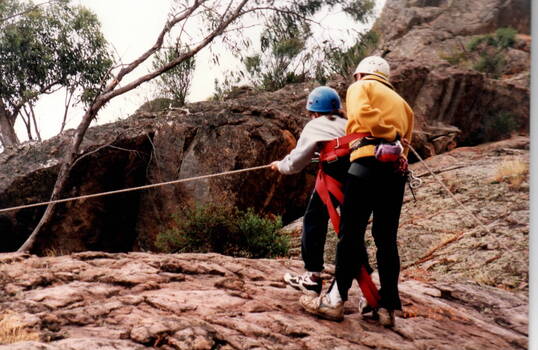 An instructor supervising a girl in rock climbing on a natural rocky outcrop.