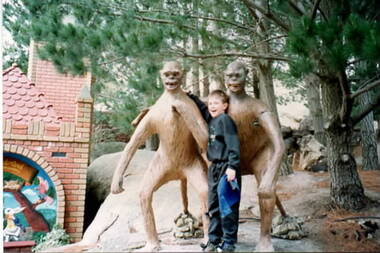 A boy standing between a sculpture of two monkeys at a park.