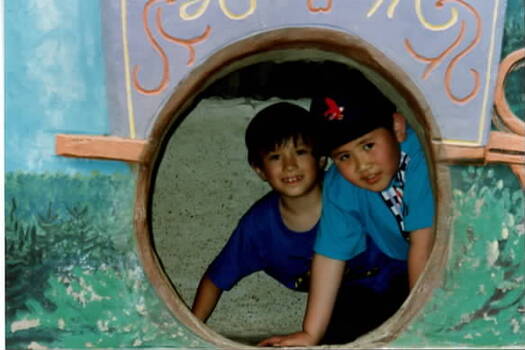 Two boys looking through a large round hole in a wall.