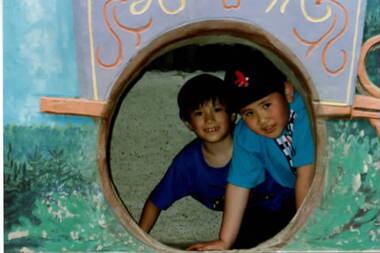 Two boys looking through a large round hole in a wall.