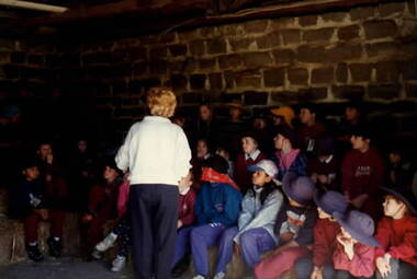 A group of children are sitting on bundles of hay in a farm building.