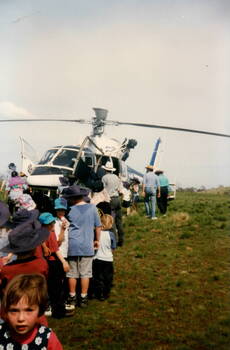 Children are lined up to see a police helicopter that has touched down in an open area.
