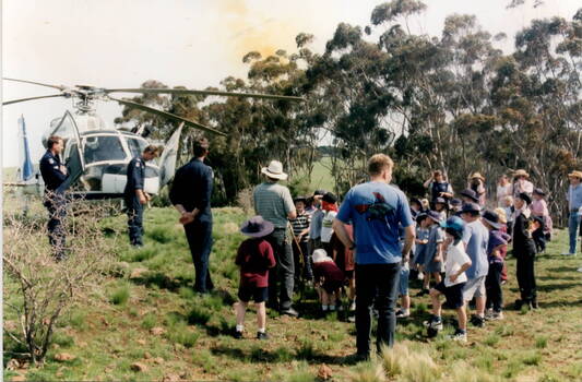 Some policemen, who arrived in a helicopter are talking to a group of children about their helicopter.