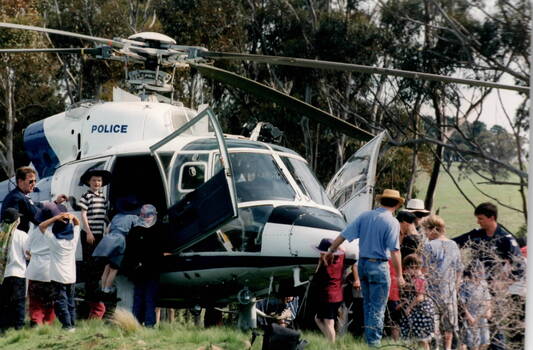 A group of children under the supervision of some adults and policemen are being shown the workings of a police helicopter.