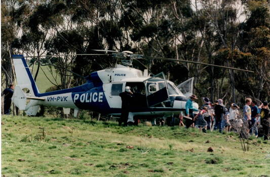 A group of children are lined up looking at a police helicopter which landed in an open area. 