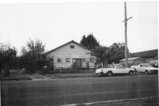 A large shed-like building with two utility trucks parked in the street in front of the building.