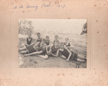 A photograph of eight young men sitting on a grassy area and dressed in swimwear c1917.