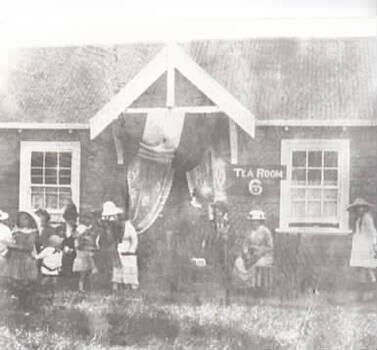 A gathering of people outside a building that is displaying a tea rooms notice. 