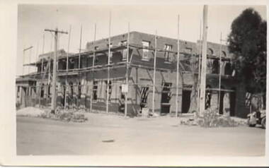 A two storey brick building is being built on a street corner. Scaffolding is surrounding the construction.