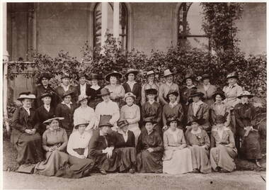 A photo of a group of well-dressed women posing for a photograph in front of a large mansion.