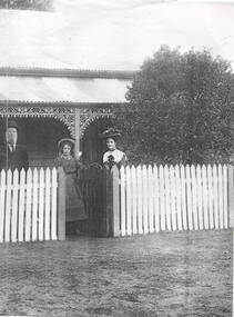 A lady, man and young girl are standing outside a weatherboard home.