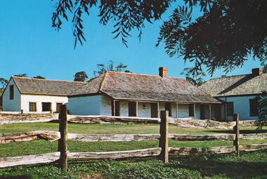 A coloured photograph of a single storey homestead with a post and rail fence across the property.