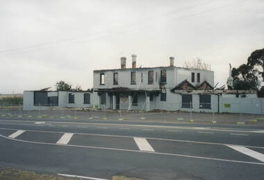 A hotel building by a roadside has been damaged by fire. The walls are intact but the roof has collapsed.