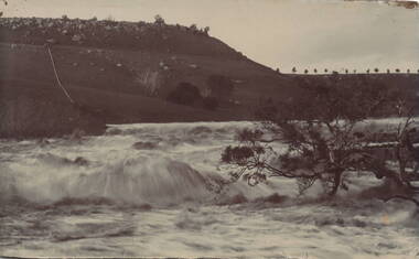 A waterfall tumbling over rocks in a river with a high escarpment rising up from the watercourse.