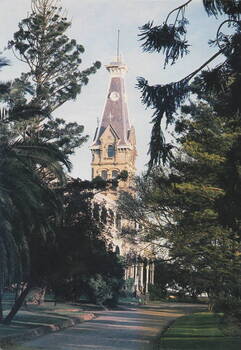 A picture of garden and a Victorian mansion with a tall tower over the main entrance.