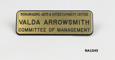 Gold coloured oblong badge with 'Nunawading Arts and Entertainment Centre /Valda Arrowsmith/ Committee of Management