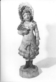 Plaster figurine of young girl in light green dress and hat with dark green boots carrying a (broken) fan.