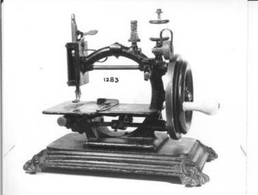 Small hand operated sewing machine with wooden handle to turn wheel which operates mechanism. 