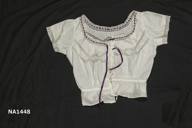 White cotton camisole with purple ribbon threaded eyelet lace at neck. 
