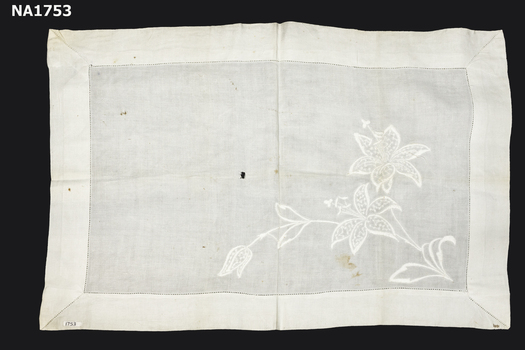 White linen tray cloth with large flower design embroidered in white.