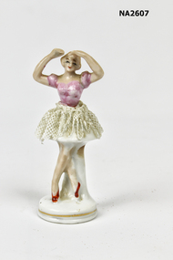 Small figure of ballerina with pink top, tulle skirt and red shoes. 