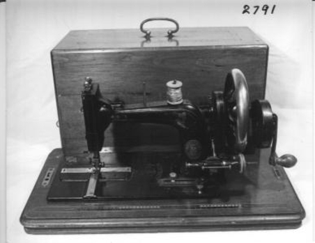 Sewing machine, hand operated with transverse shuttle, spool wound by running on to a large wheel. 