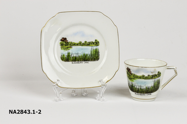 White cup and saucer with gold edges and a scene of Blackburn Lake.