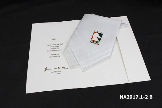 White cotton handkerchief with gold inscription folded into a white inscribed card.