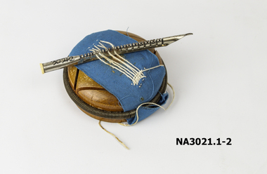 Round wooden block with sample of material to demonstrate how to use the darner and needles.
