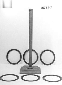 A wooden pole and square base and six green metal rings.