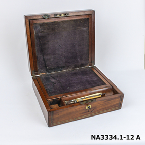 A square wooden box with brass inlay decoration on lid and front around lock. 