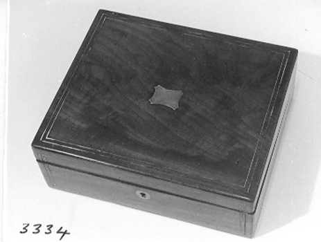 A square wooden box with brass inlay decoration on lid and front around lock. 