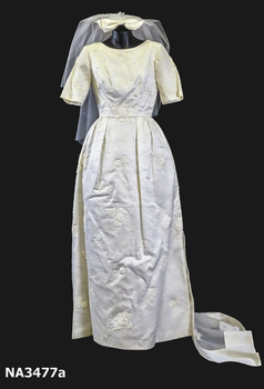 1963 Wedding dress of cream satin; floor length, short sleeves, round neckline, fitted at waist.