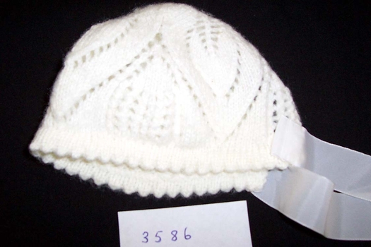 A 1964 creamy white knitted bonnet, pattern in the shape of petals from the centre at the back of the head.