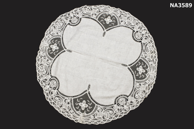 A round cloth, white with tape lace border attached to scalloped white linen.