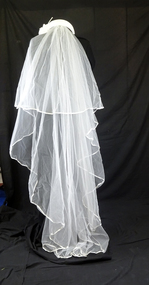 Wide, white 1978 headband padded and covered with nylon net, and decorated with satin flowers. Veil trimmed with 4 cm wide satin ribbon