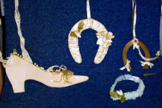 Pale pink cut out shoe designed to be worn on arm of bride . With two decorated horshoes in white and cold and blue garter. 