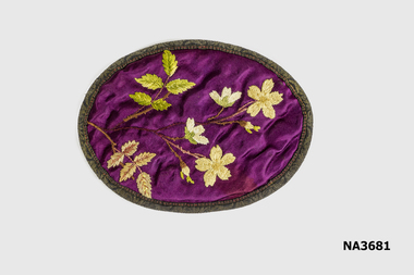 Oval piece of hand embroidery. Yellow flowers and two sets of leaves on purple silk background. 