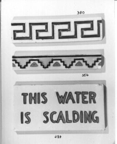 White glazed rectangle tile engraved in orange writing 'This Water is Scalding'