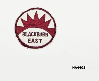 Round material school badge. Cream/Maroon edge on maroon rising sun and Blackburn East printed under the sun in black.